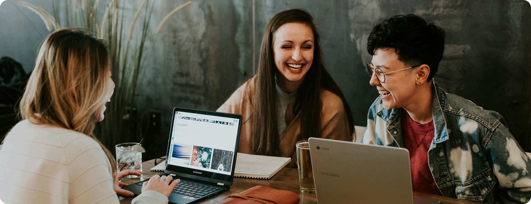 Three smiling people gathered around laptops